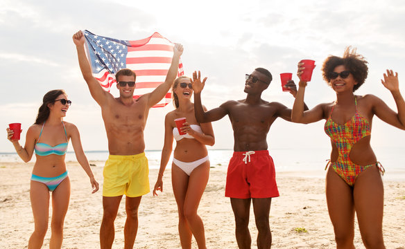 summer, holidays and people concept - group of happy friends with flag and non alcoholic drinks celebrating american independence day and party on beach