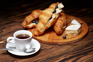 Cup of coffee with croissants, Camembert cheese, blueberries on a wooden background.
