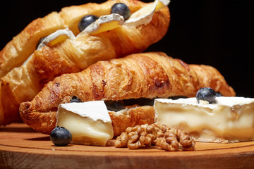Croissants with Camembert cheese and blueberries on a dark background. Place for text, copy paste.