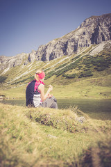 Junge blonde Frau rastet am Ufer eines Bergsees, Österreich
