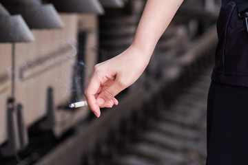 In the photo, a woman's hand holds a lit cigarette.