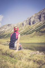 Junge blonde Frau rastet am Ufer eines Bergsees, Österreich