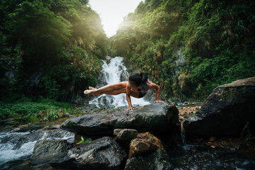 Young woman practice yoga near waterfall in forest