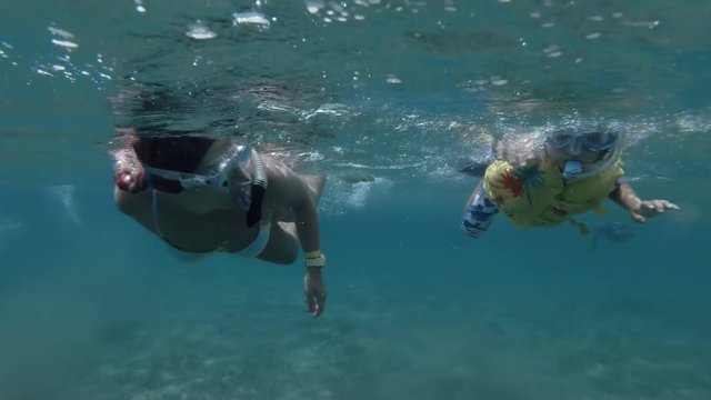 Woman and little boy in mask, snorkel and fins swim on the surface of water (underwater , Low-angle shot, 4K / 60fps)
