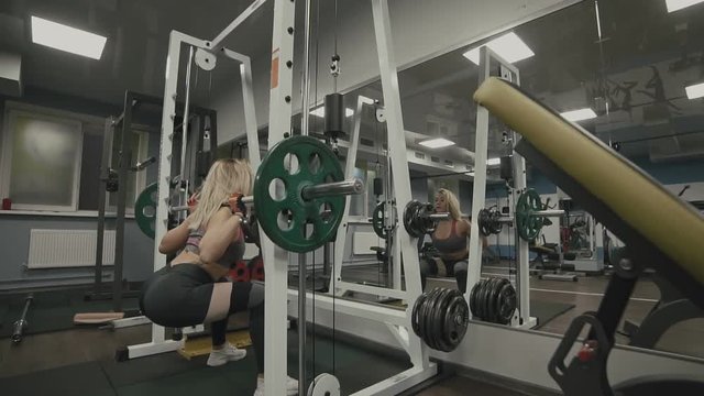 Beautiful sporty woman in gray sportswear doing squat workout in gym in slow motion. Healthy lifestyle concept. Wide angle
