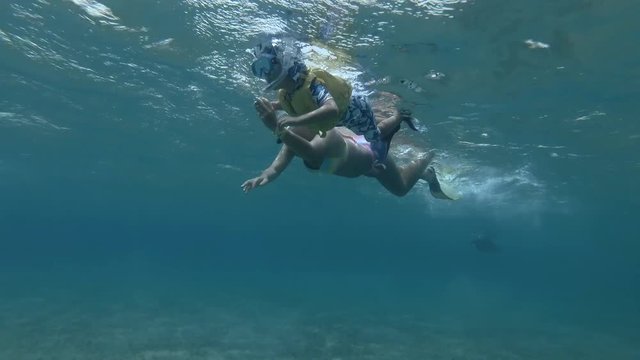 Woman and little boy in mask, snorkel and fins swim on the surface of water (underwater , Low-angle shot, 4K / 60fps)
