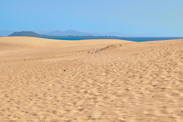 Spectacular paradisiacal landscape of golden sand dunes and blue sea with mountains in background in Corralejo Natural Park, Fuerteventura, Canary Islands, Spain