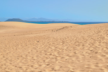 Spectacular paradisiacal landscape of golden sand dunes and blue sea with mountains in background in Corralejo Natural Park, Fuerteventura, Canary Islands, Spain