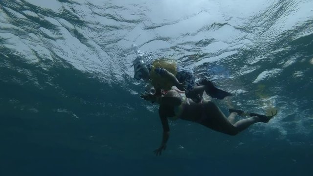 Woman and little boy in mask, snorkel and fins swim on the surface of water (underwater shot, 4K / 60fps)
