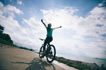Hands free cycling woman riding Mountain Bike on sunrise seaside