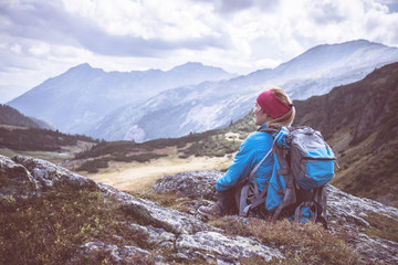 Junge blonde Frau sitzend in den Bergen, Blick in die Ferne, Abenteuer