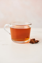 Close up of black tea in a glass cup with anise on marble table top. Feminine rose background with copy space. Narrow depth of field.