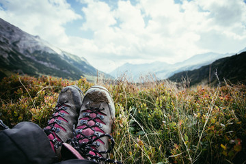 Wanderstiefel einer jungen Frau im Almgras, unscharfe Berglandschaft im Hintergrund 