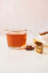 Black tea in a glass cup with golden spoon with herbs, dipper and anise on marble table top. Feminine rose background with copy space. Narrow depth of field.