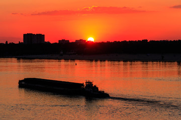 Tugboat pushing a heavy long barge on the river Dnieper at sunset