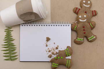 Ginger bread cookies on craft paper background . Blank notepad with leaf of fern. Coffee Christmas mockup. Top view.