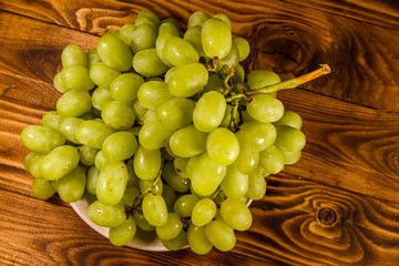 Ceramic plate with green grapes on wooden table. Top view