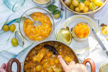 Plum jam in the pot and woman puts it to jars, food and healthy eating concept