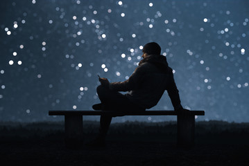 A man is sitting on a bench and using a smartphone. Starry sky bokeh In the background