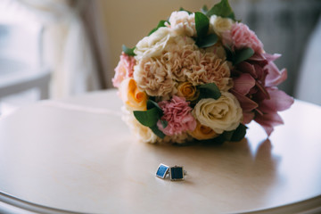 Close-up a cufflinks and a wedding bouquet on a white table. Clothing accessories for businessman...