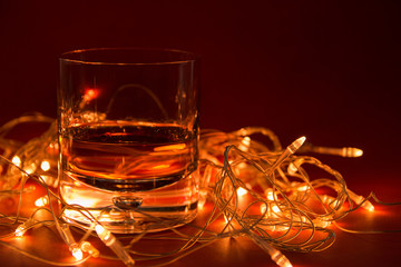 a glass of whiskey and in the background a glowing garland on a red background with a copy of space