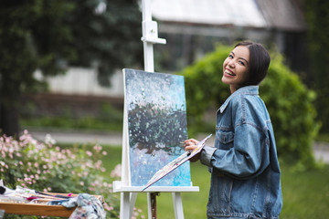 Portrait of young talented female artist making sketches with brightful oils, drawing on easel,...