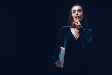 vampire woman showing silence symbol and holding magic book isolated on black
