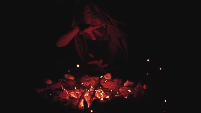 Scary witch does voodoo black magic ritual near the fire at night. Halloween horror 