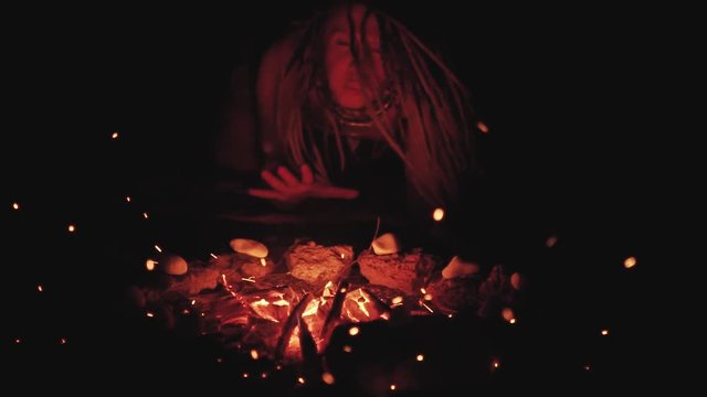 Scary witch does voodoo black magic ritual near the fire at night. Halloween horror 