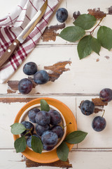 Fresh plum berries on a plate with leaves on a light table.