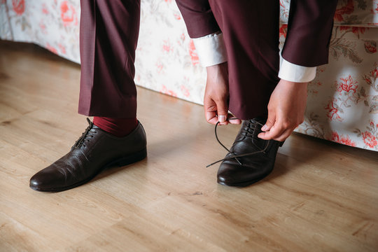 Close-up hands of a man tie laces on black shoes. A businessman in burgundy trousers and socks wears shoes before going to work in the office. The concept of fashion clothing and shoes.