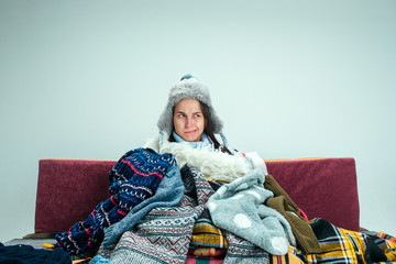 The young sick woman with flue sitting on sofa at home or studio covered with knitted warm clothes....