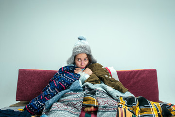 The young sick woman with flue sitting on sofa at home or studio covered with knitted warm clothes....