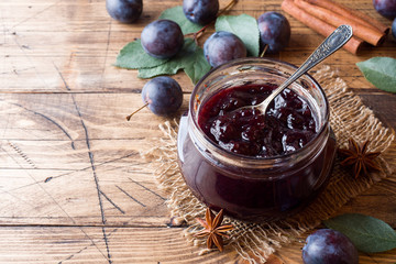 Plum jam in a glass jar. Fresh plum fruit on a wooden table.