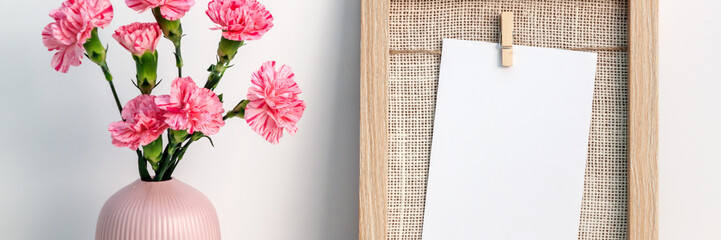 A panoramic photo of with wooden frame mockup and pink carnations in a notched vase