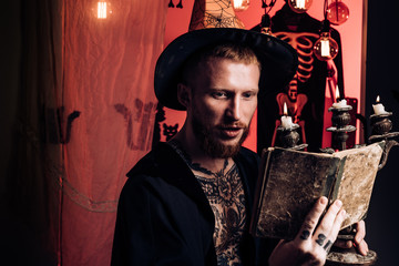 Red-haired man reading a magic book with spells. Happy father on halloween background with magik...