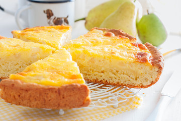 Pie from the cottage cheese pastry with pear and sour cream, cut into pieces on a white table, horizontal