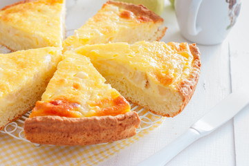 Pie from the cottage cheese pastry with pear and sour cream, cut into pieces on a white table, horizontal