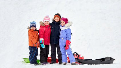 childhood, friendship and season concept - group of happy little kids with sleds hugging in winter