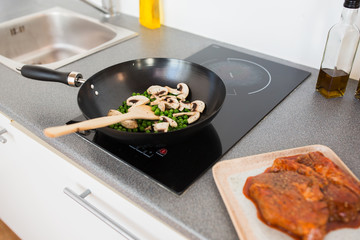 food, culinary and cooking concept - close up of mushrooms with pea in frypan on cooker