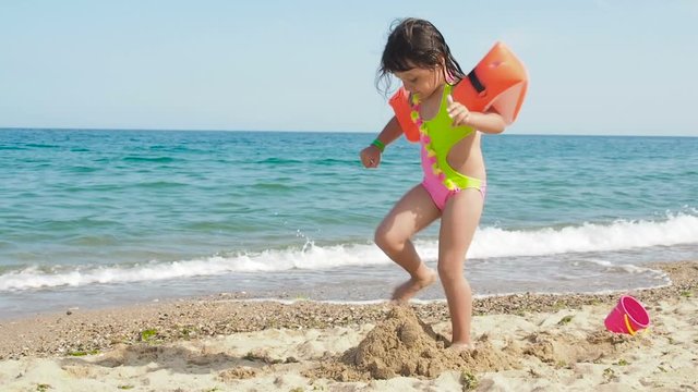 Child on the beach. A little girl destroys sand castles.