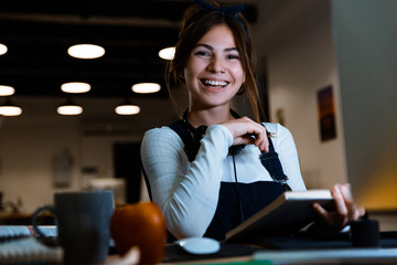 Woman designer sitting in office working reading book taking notes at night.