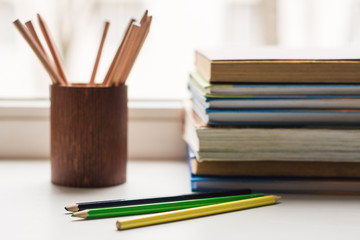 A stack of old books and several different colored pencils lie on the windowsill, a couple of pencils lie ahead