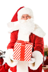 santa claus holding striped gift box and looking at camera isolated on white