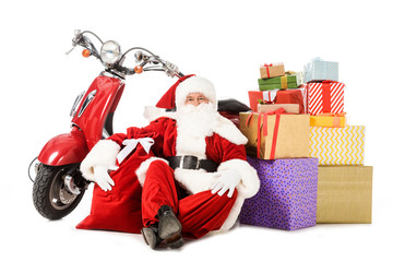 tired santa claus sitting on floor with vintage red scooter, sack and gift boxes isolated on white