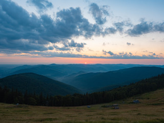 Background of Carpathians mountains, west Ukraine. The sun on horizon, dense clouds in evening sky, dark mountain range covered with woods. Ukrainian nature landscape in august. Blurred background