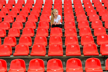 lonely young woman sitting in armchair at stadium