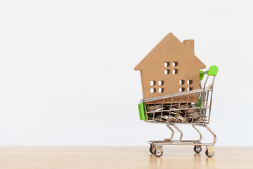 House model in mini shopping cart with stack of coins money on wooden table for residential investment. Concept for property ladder, mortgage and real estate investment