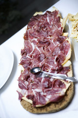 Vassoio di prosciutto tagliato finemente a fette sopra una sfoglia di pane carasau  in un vassoio di sughero