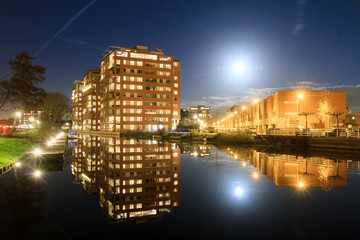 Modern new residential district in Leiden, The Netherlands, with apartment buildings reflected in the water at night, with a full moon
